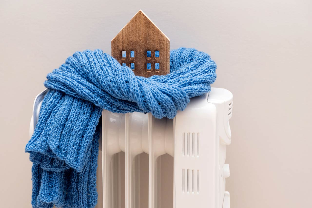 Wooden model house wrapped in a blue scarf on a radiator